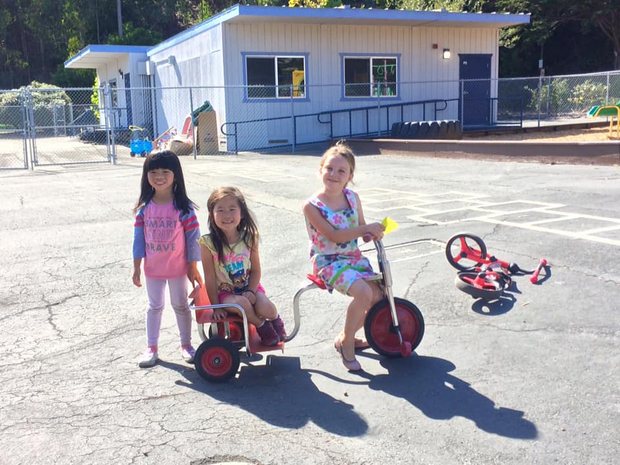 Children riding tricycles on the play area outside the Mills Montessori classrooms